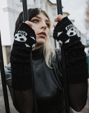 Model wearing chunky knit black gloves with white skull and crossbones